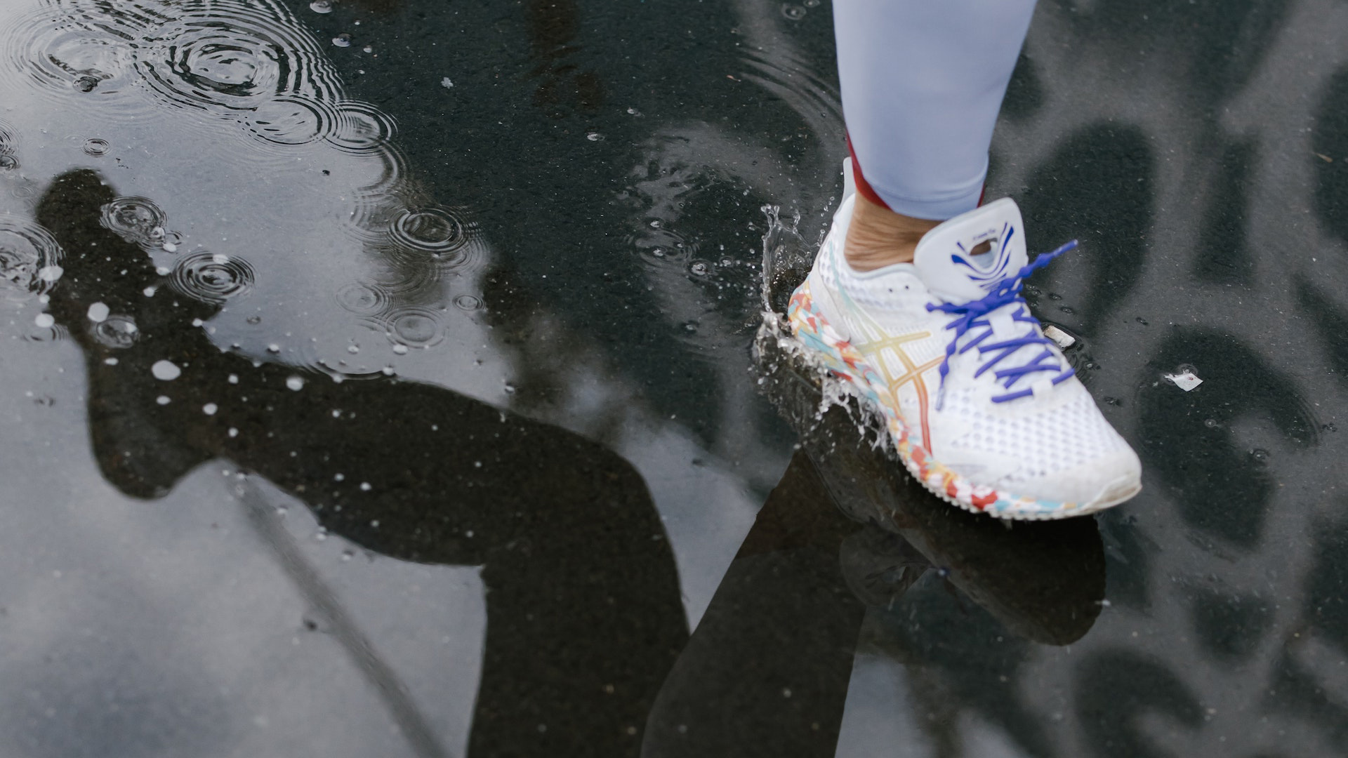 Close up of a foot in a running shoe on wet ground with the reflection of the person's other leg