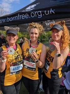 Three women in Born Free running vests and animal pattern ears holding up medals