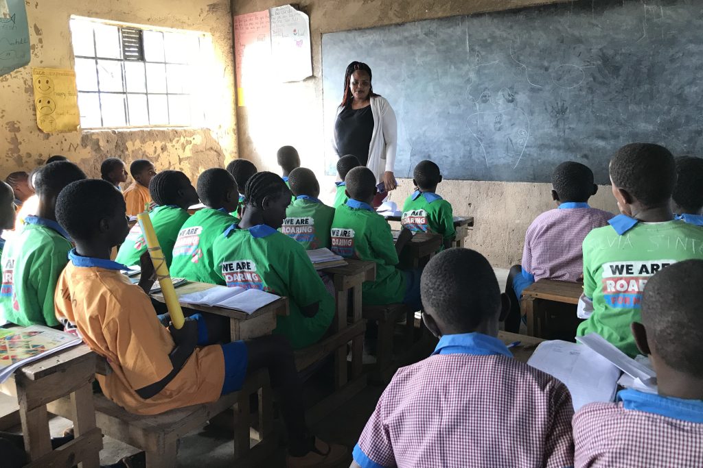 Kenyan students in a classroom with a teacher stood in front of a blackboard