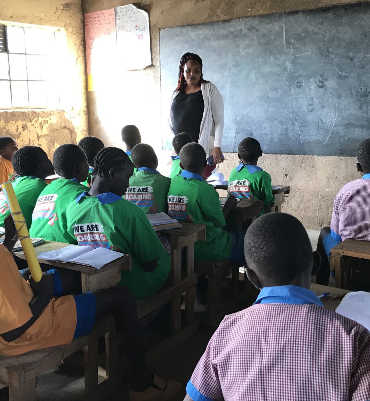 Kenyan students in a classroom with a teacher stood in front of a blackboard