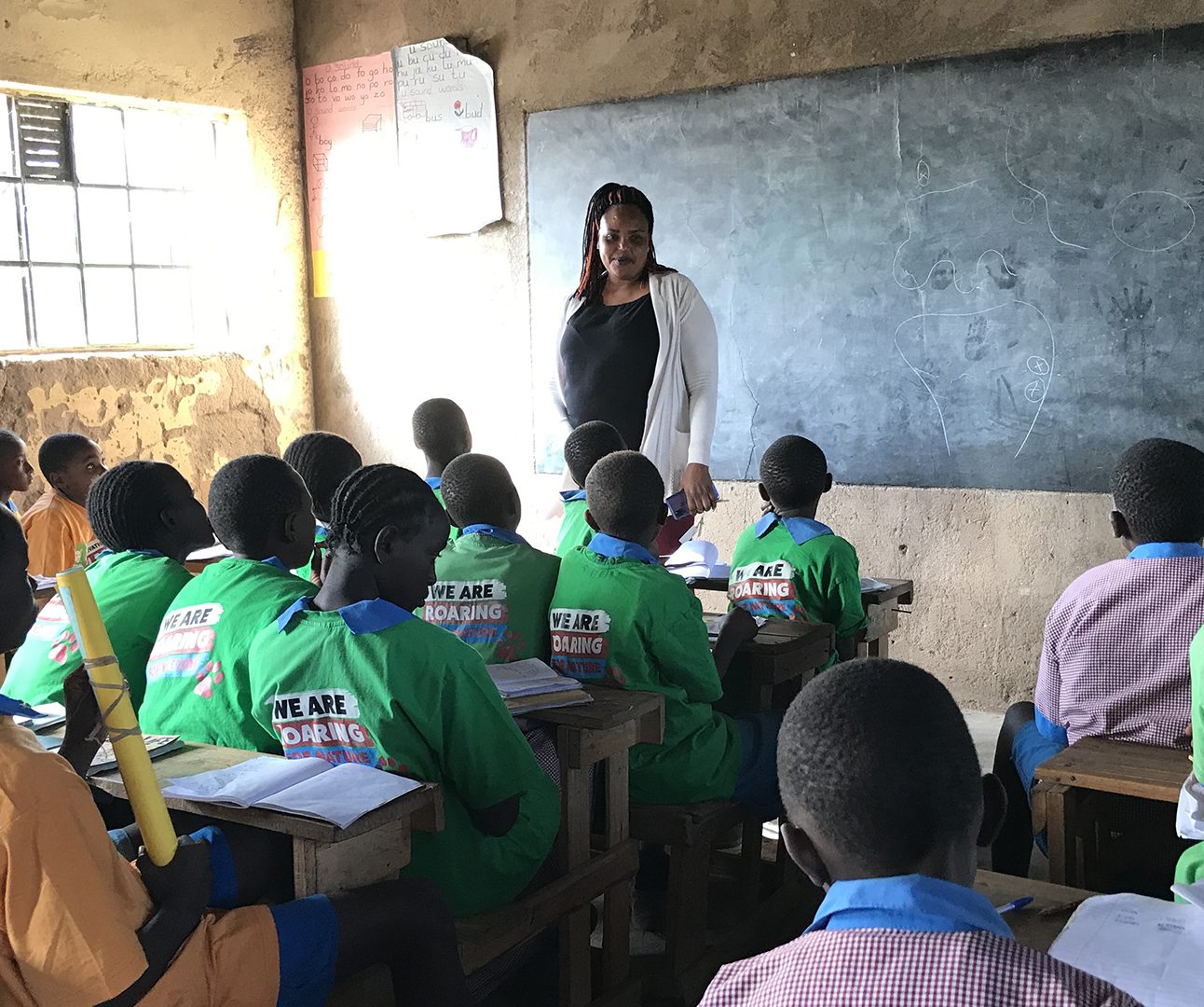 A class full of Kenyan school children wearing green Born Free t-shirts, looking at a teacher in front of a chalk board