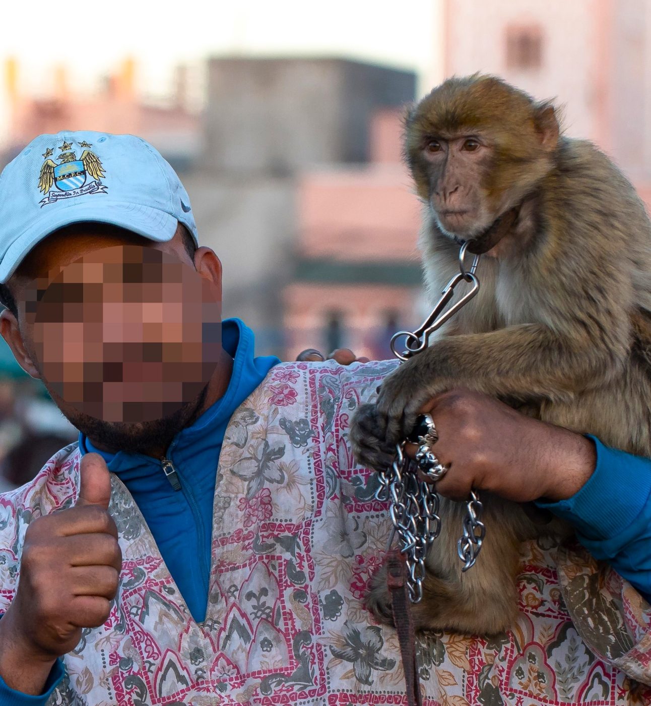 A macaque sits on the shoulder of a man posing for a photo with a chain around its neck