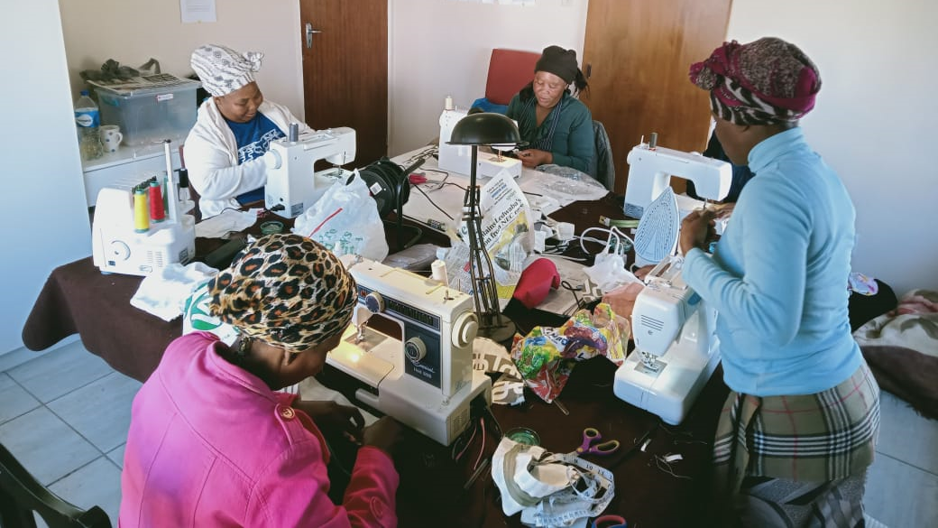 A group of women sit around a table, using sewing machines