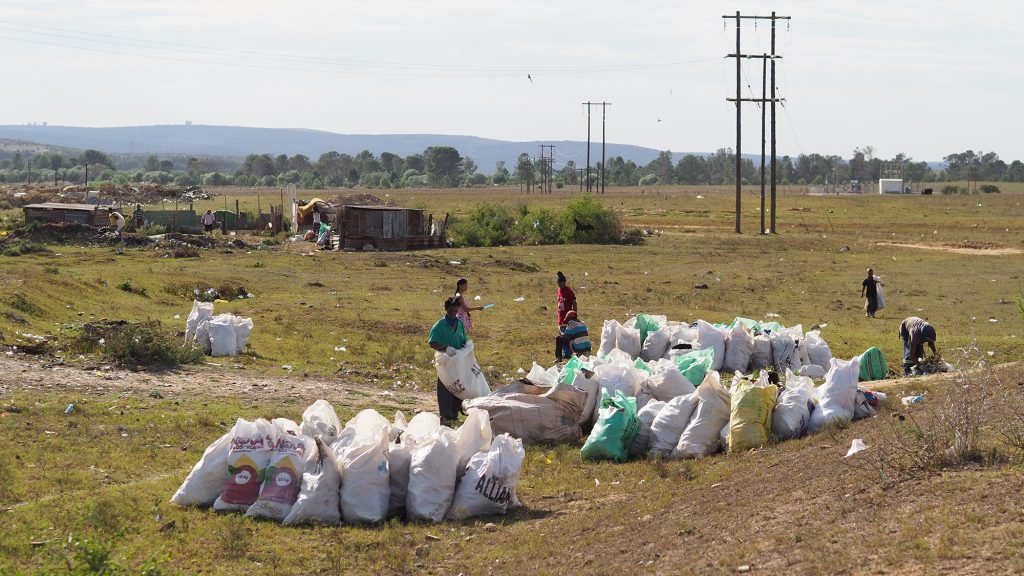 Lots of large rubbish bags are piled together, with people collecting more rubbish around them