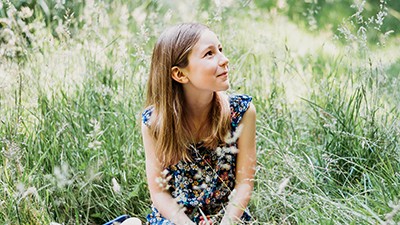 A photo of Thea Caine sitting in a field of long grass