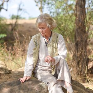 Virginia McKenna sitting on the ground under a tree at the grave of Elsa the lioness