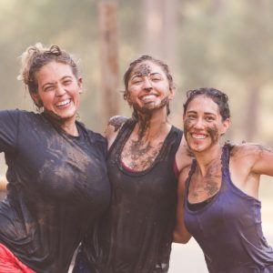 Three women celebrating, covered in mud