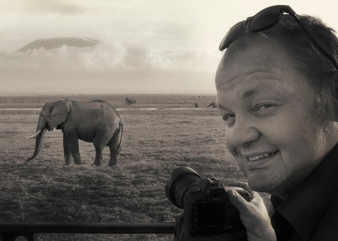 Black and white photo of George Logan holding a camera with an elephant in the background