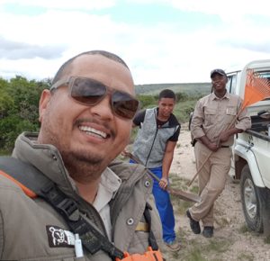 Three men are posing for a photo, stood by a truck holding work tools