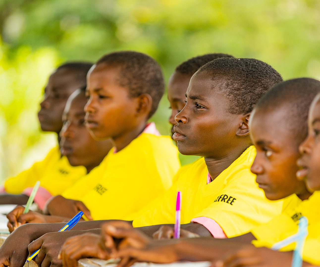A row of Kenyan school children are sitting at a desk in yellow t-shirts with the Born Free logo