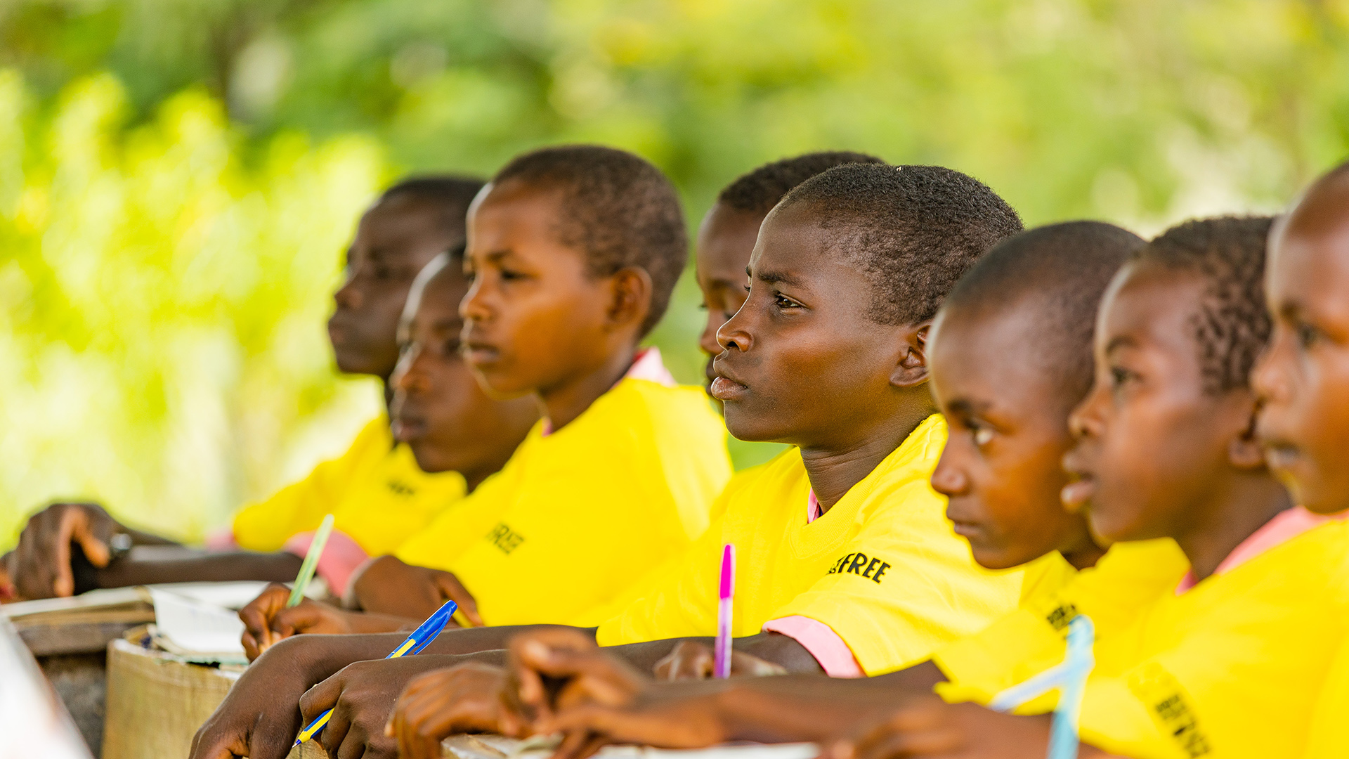 A row of Kenyan school children are sitting at a desk in yellow t-shirts with the Born Free logo