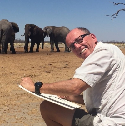Jonathan Truss with a sketch book in front of a group of elephants