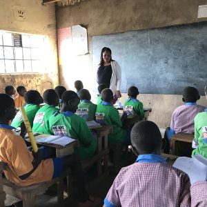 Children in a classroom facing a teacher stood in front of a blackboard