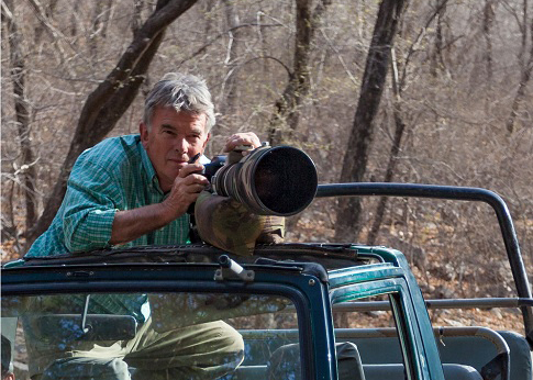 Michael Vickers leaning out the top of a car with a camera