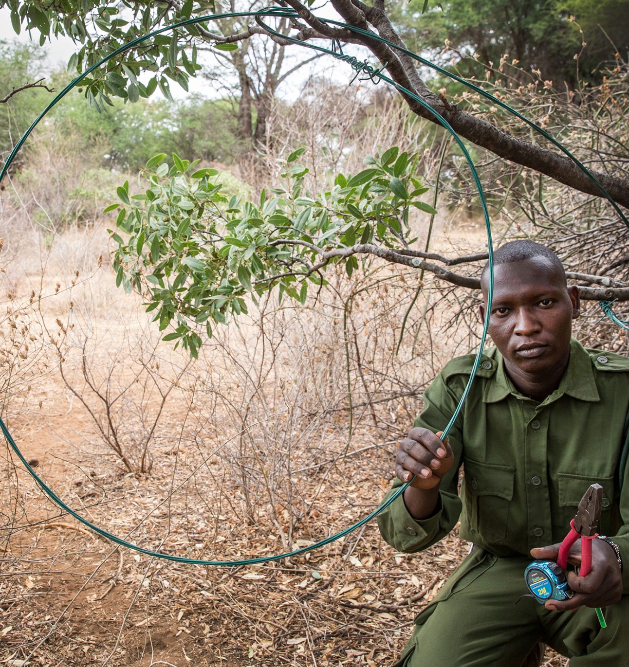 A man in green ranger uniform holds up a circular wire snare, also holding a pair of flyers