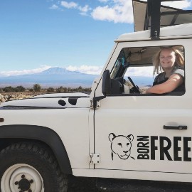 A blonde haired woman in a white born Free landrover, with mount Kenya in the background