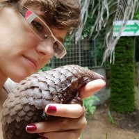 A photo of a white women holding a pangolin, she is wearing glasses and looking at the pangolins face.