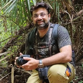 A photo of Kedar Gore crouching in the jungle holding a camera