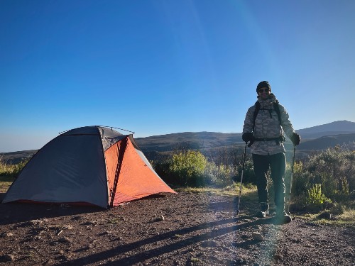 A man stands next to a tent on the mountain
