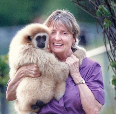 A woman wearing a purple top, standing holding a primate in her arms.