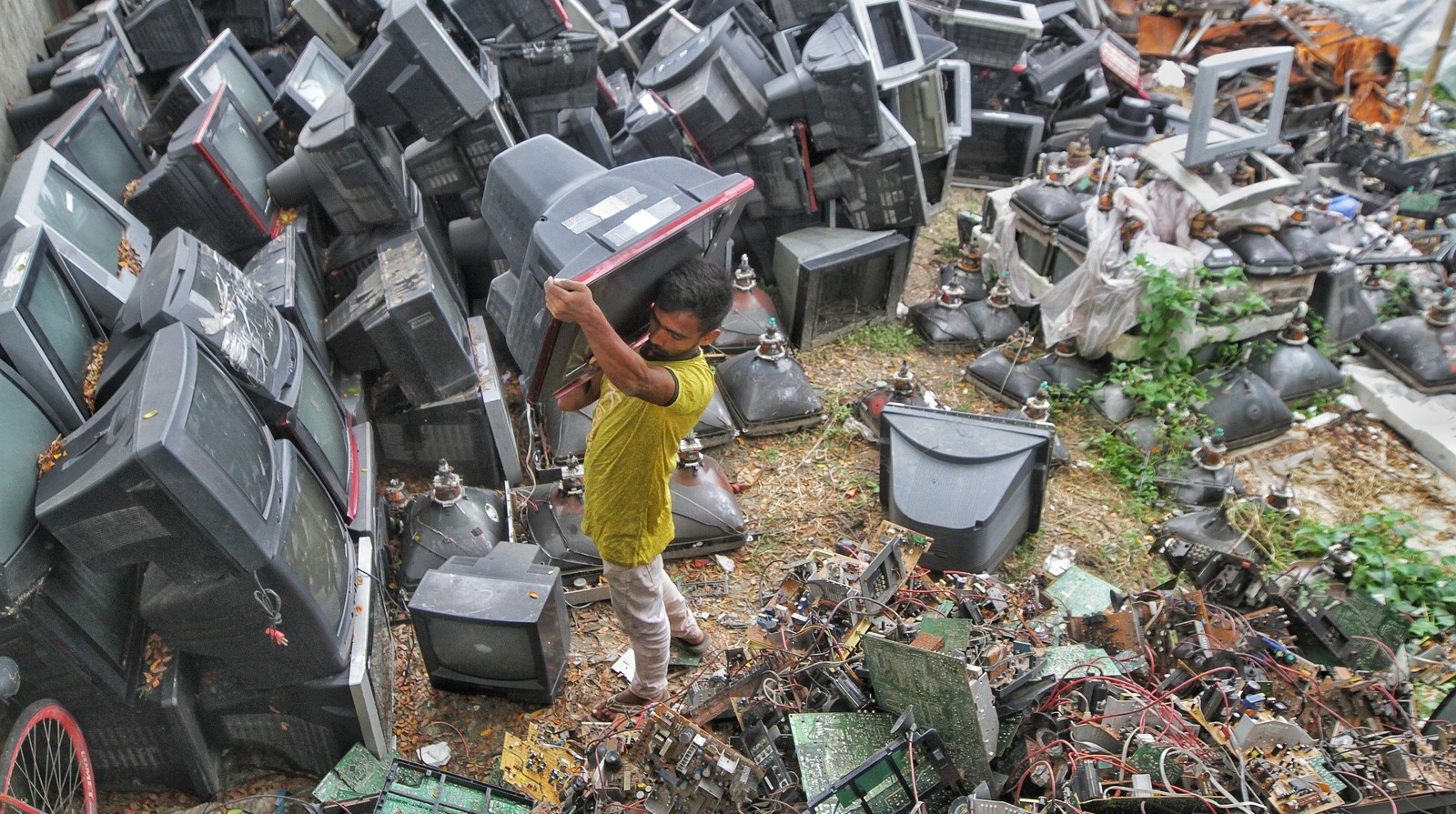 A man carries a television through piles of dumped electrical items