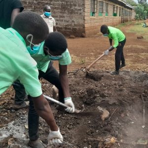 Students wearing masks and gloves digging out the waste pit