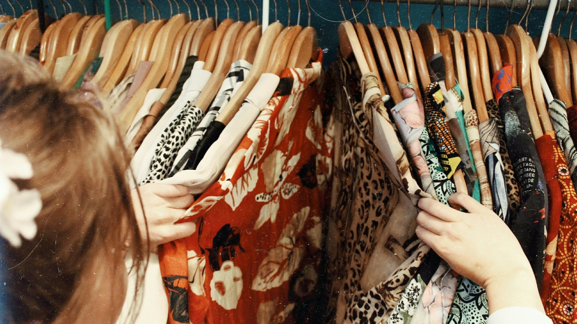 A rail of colourful shirts and blouses on wooden hangers