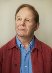 A headshot of Michael Morpurgo in a blue shirt and red jacket