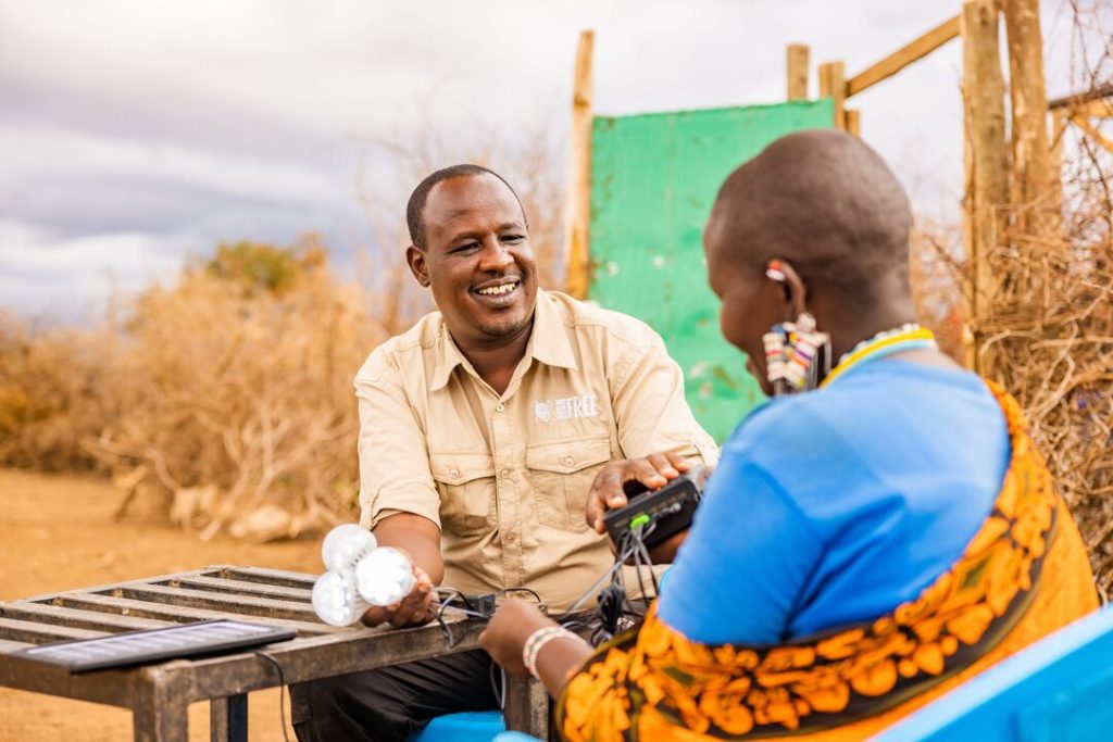 A man wearing a Born Free uniform standing with a woman in traditional Maasaii dress, looking at solar lighting 
