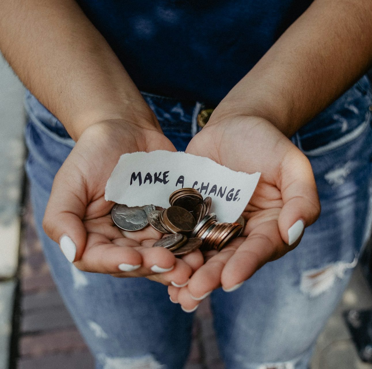Close up of a person's cupped hands holding lots of coins, with a piece of paper saying 'make a change'