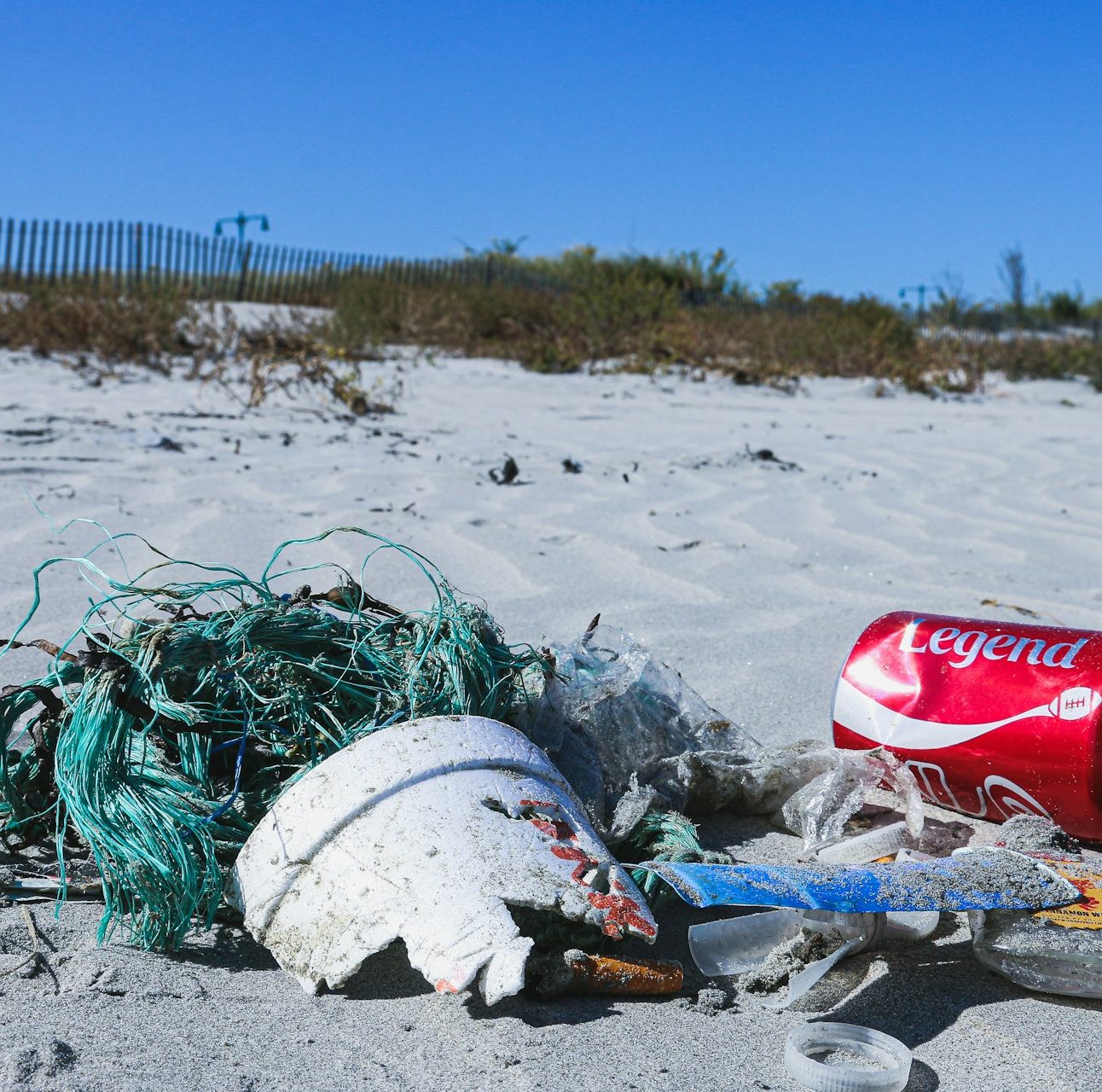 Close up of a pile of litter on the beach, including a coca cola can, fishing netting and broken pot