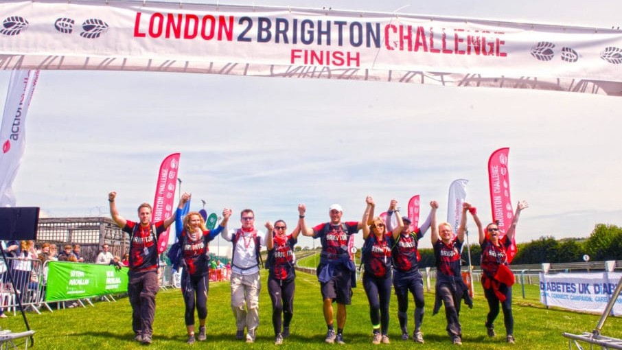 A group of people linking hands triumphantly, as they cross the finishing line of a challenge event