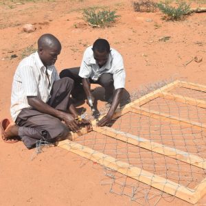 Two men constructing part of predator-proof boma, by fixing wire to a wooden frame.