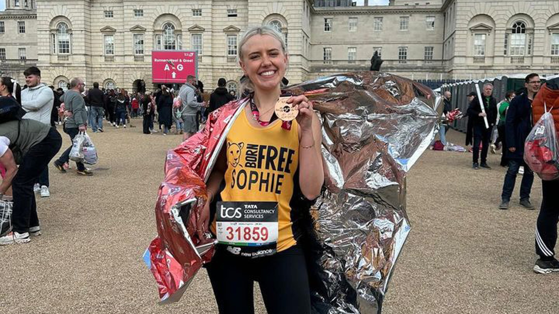 A woman wearing a Born Free running vest, holding a London Marathon medal, wrapped in a foil blanket
