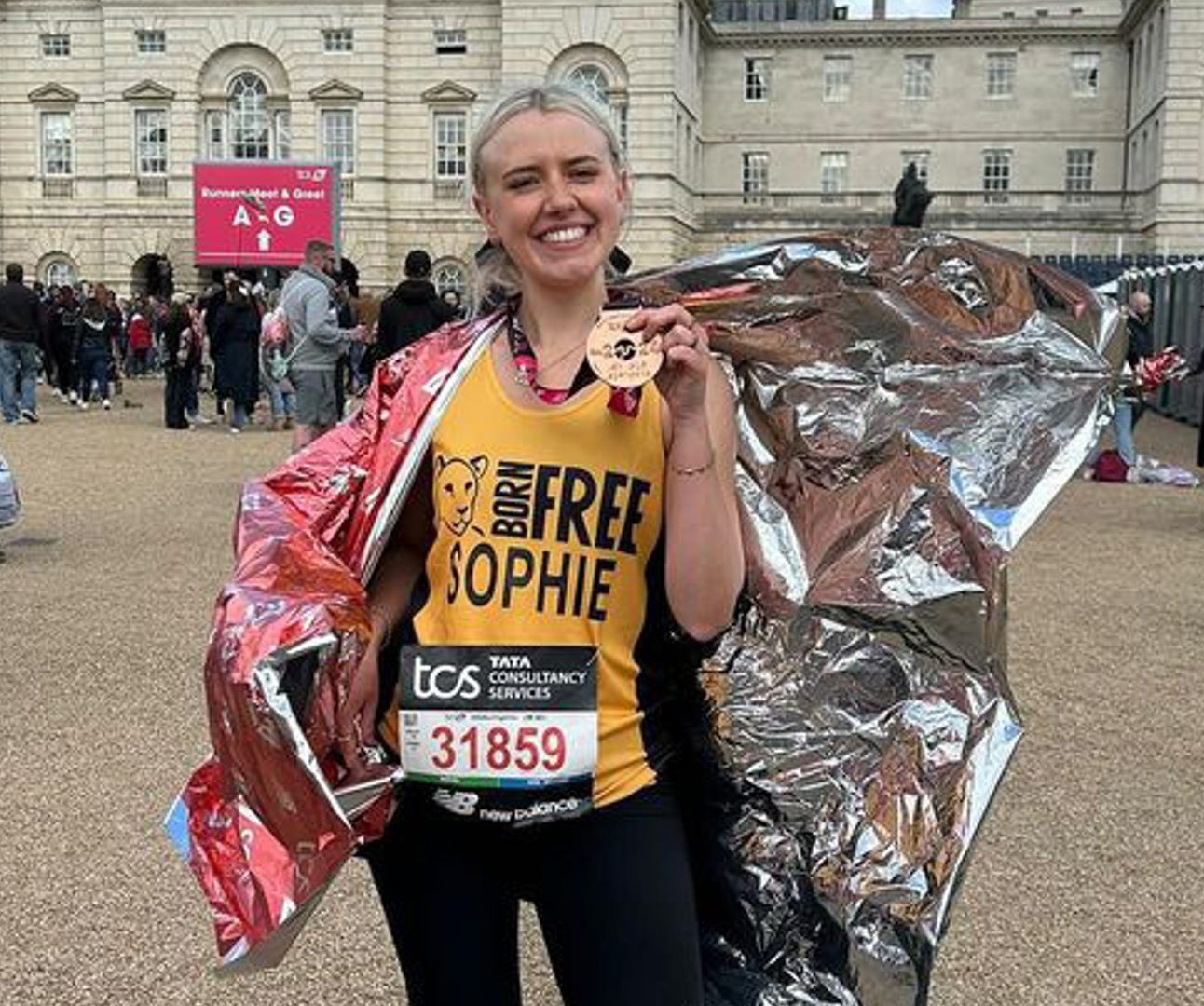 A woman standing at the finishing line of the London Marathon holding her medal