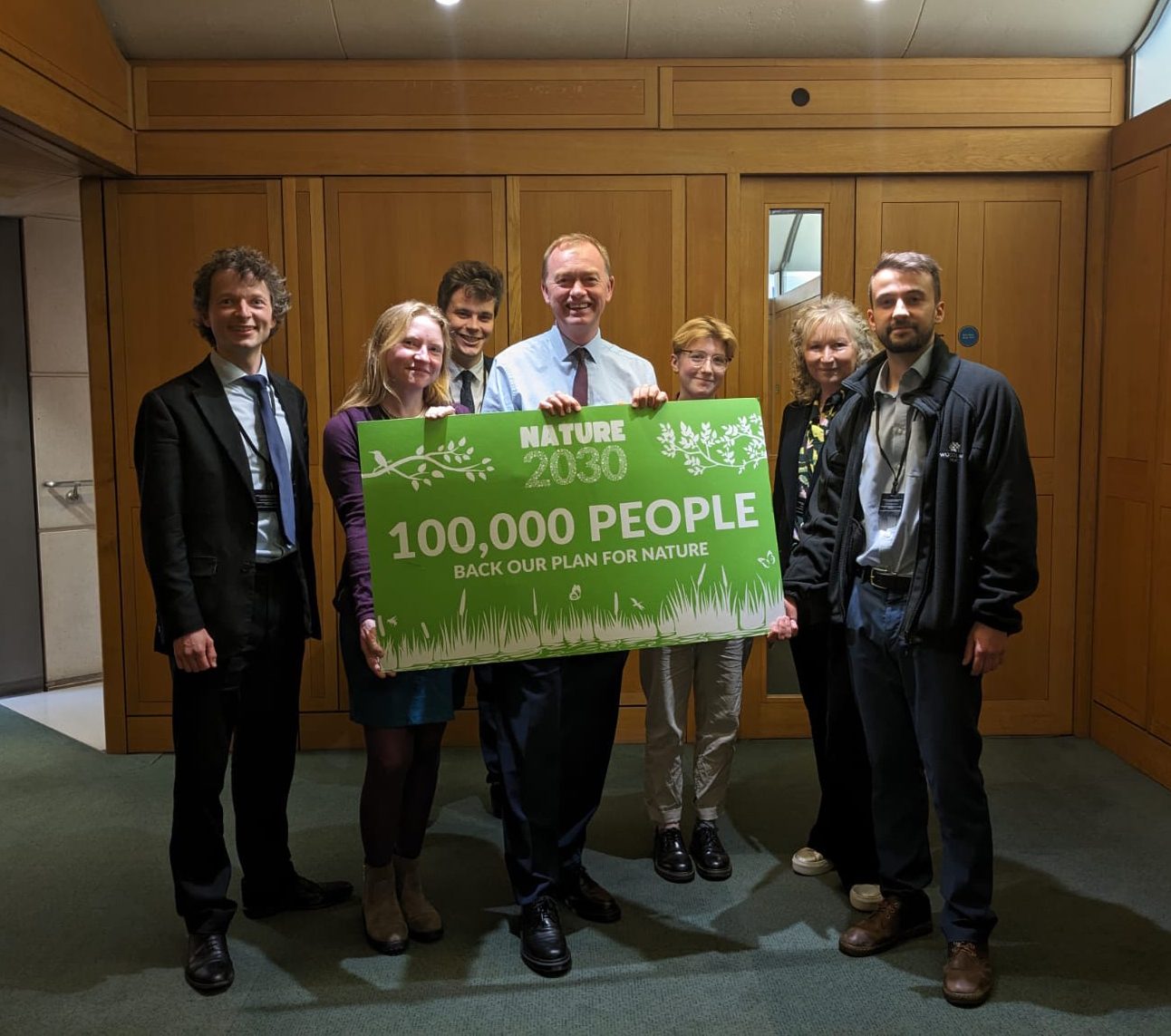 A group of people in an office, holding a large sign saying 'Nature 2030: 100,000 people back our plan for nature'