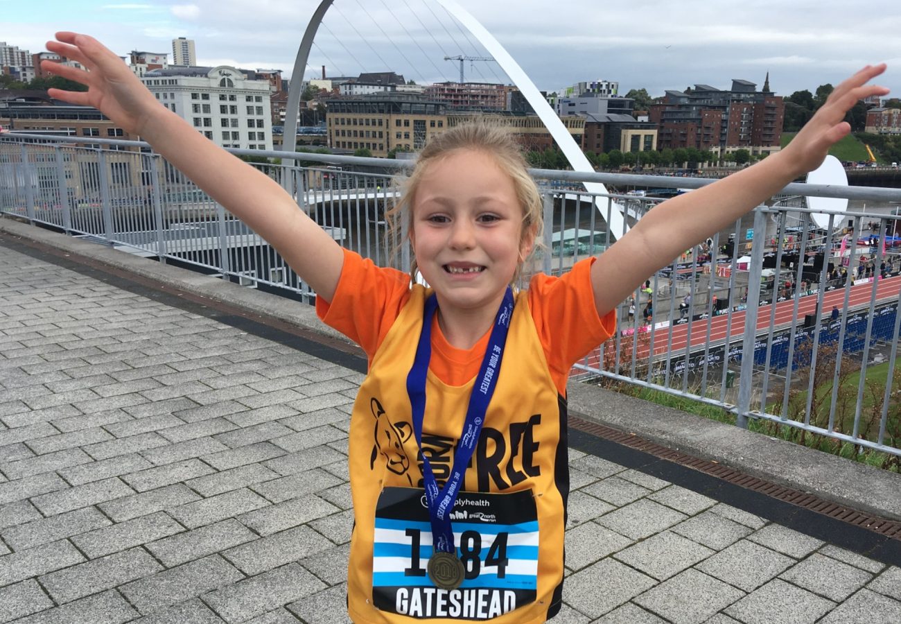 A young girl with her arms outstretched, with a medal around her neck and wearing a Born Free running vest