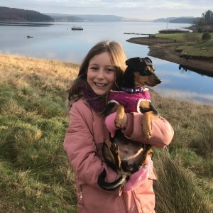 A young girl holding a small dog with lakes and mountains in the background