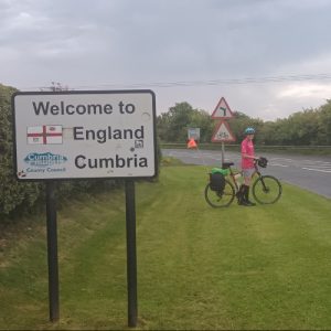 A young man on a bike next to a sign which says 'welcome to England'