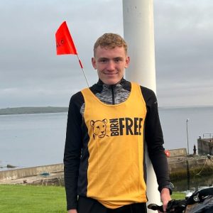 A young man standing by the coast wearing an orange Born Free vest
