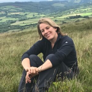 A photo of Lauren St John sitting on a hillside with the countryside in the background