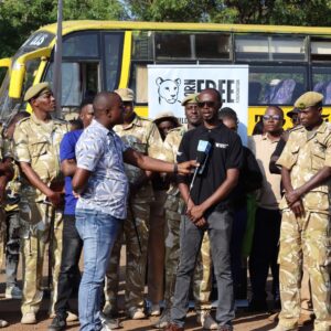 A group of people standing in front of a large yellow bus. A member of the Born Free team is being interviewed.