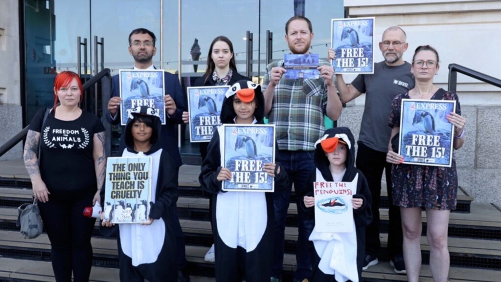 A group of people stand outside Sea Life London Aquarium holding posters.