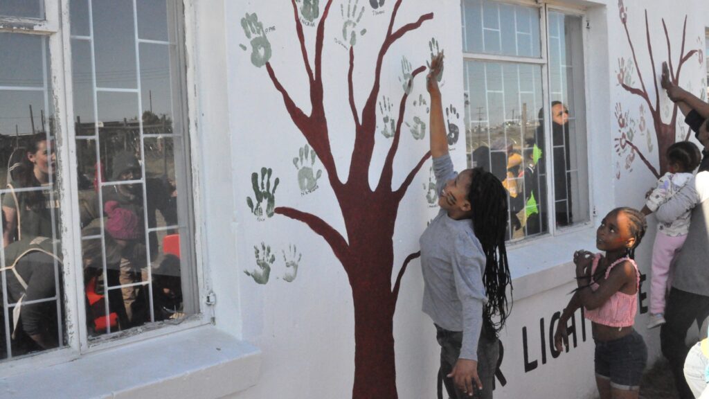 A group of children using handprint paining to create a picture of a tree on a white wall