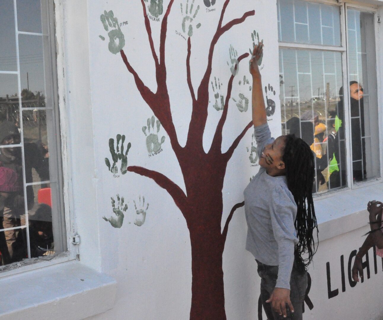 A group of children using handprint paining to create a picture of a tree on a white wall