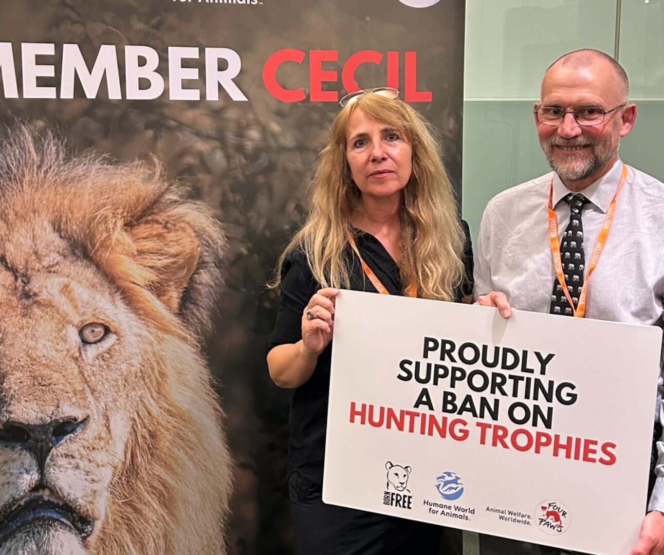 Two people standing in front of a banner with a lion's face and the words 'Remember Cecil'