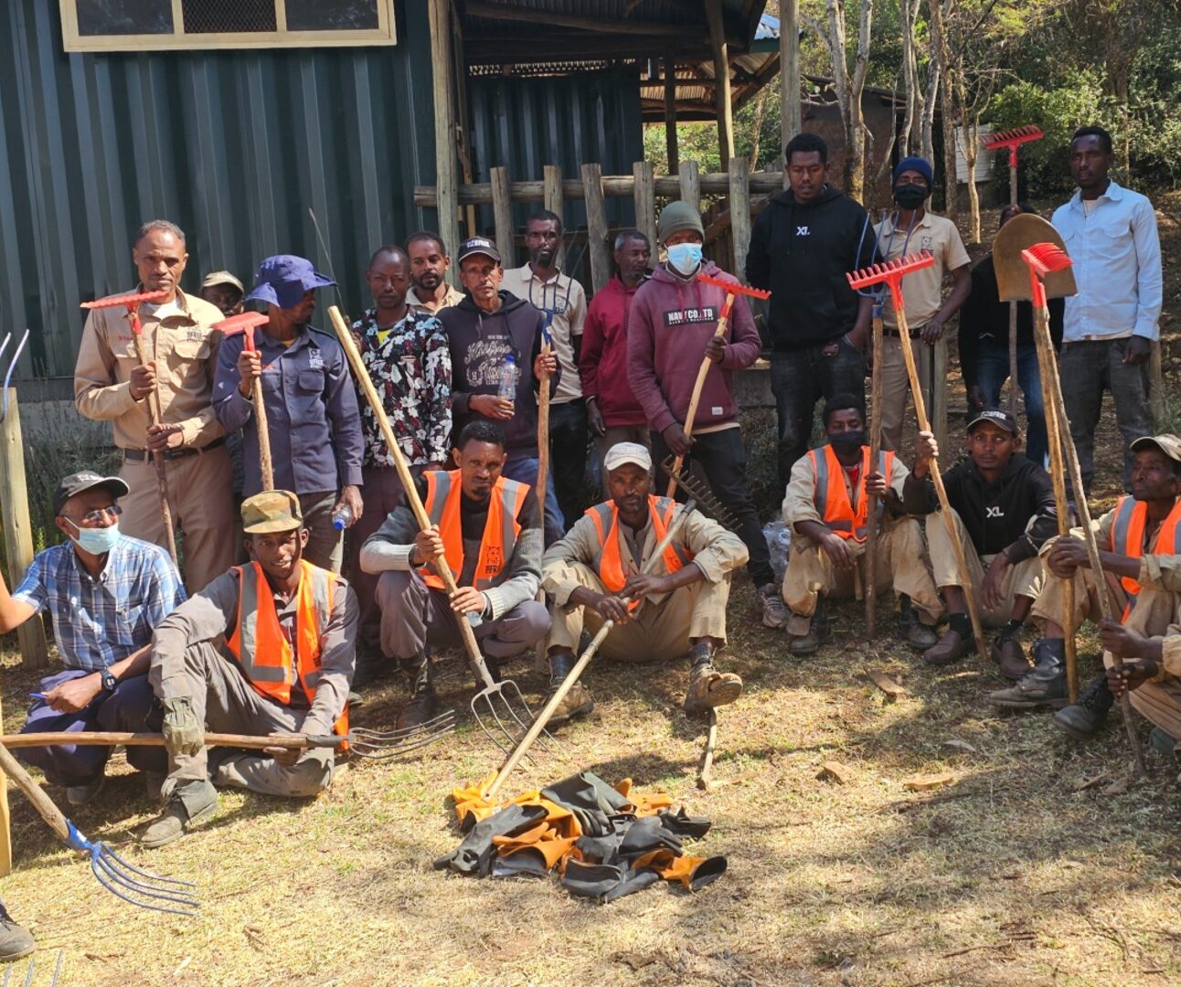 A group of people wearing high-vis vests gather, holding tools
