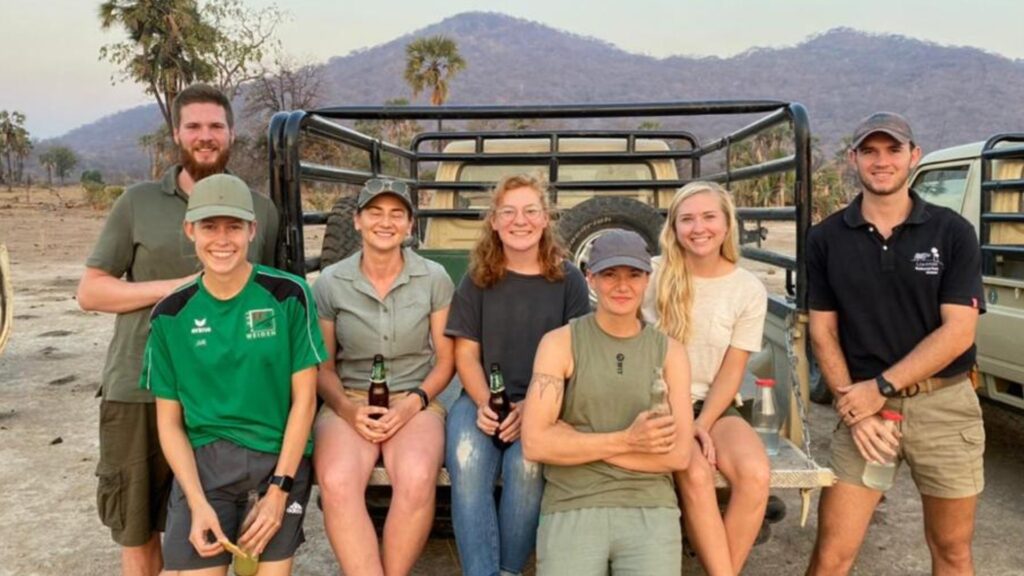 A group of people sitting on the back of a truck, with an African landscape in the background