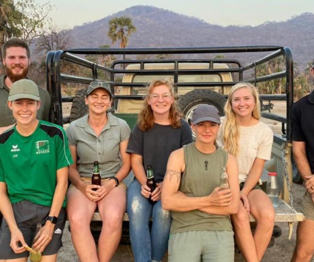 A group of people sitting on the back of a truck, with an African landscape in the background