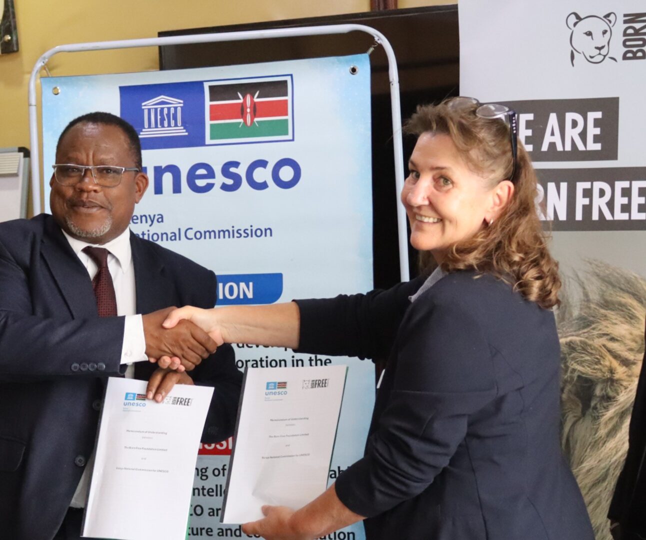 Karen Botha shakes hands with Dr James Njogu in front of a Born Free banner